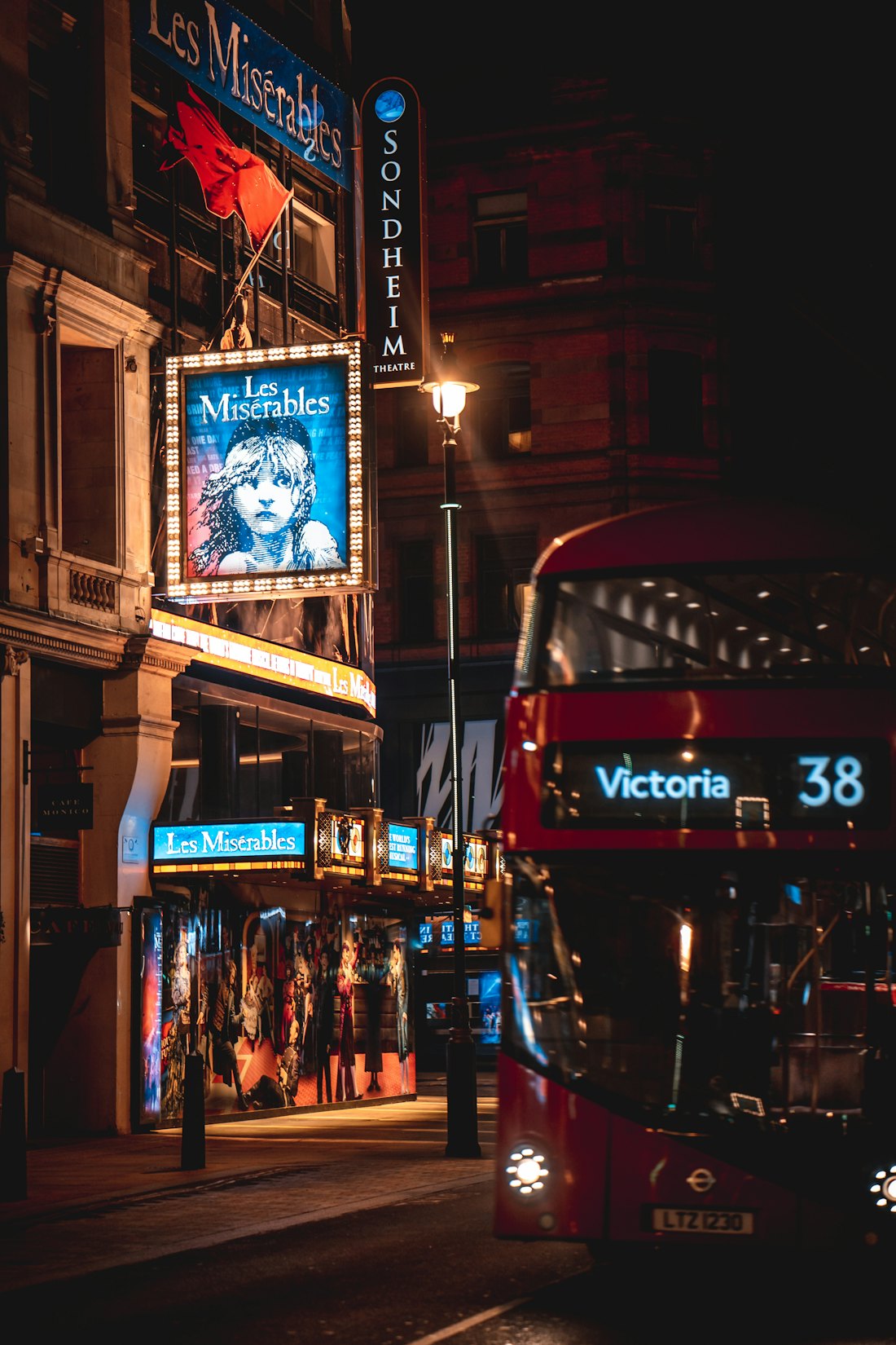 A red double-decker bus passing theatres in London's West End at night